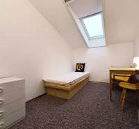 A simple room with a single bed, a table, and a dresser in a family house.