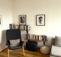 Living room with an armchair, a bookshelf full of books, pictures, and a floor with a wooden decor.
