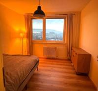 Bedroom with a table in a 3-room apartment, with a wood-patterned floor and a view from the window.