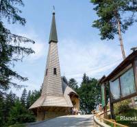 The church in the recreational grounds of Litmanová surrounded by trees and an information board.