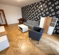 Living room in a three-room apartment with a wooden-patterned floor, patterned wallpaper, and furniture.