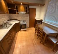 A kitchen of a 3-room apartment with wooden decor cabinets and dining seating.
