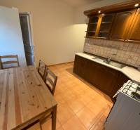 A kitchen in a 3-room apartment with a table and wooden cabinets, flooring with a wood decor.