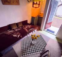 The interior of a cottage with a sofa, dining table, and open doors to the garden.