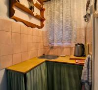 A kitchen in a cottage with wooden decor, a shelf, and a curtain by the window.