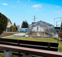 A garden in Partizánske with a greenhouse, grass, and a small flowerbed.