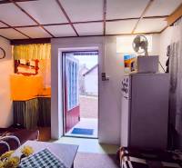The interior of a cabin with a kitchenette, a sofa, and open doors to the garden.
