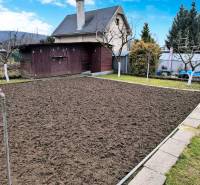 A garden with a cottage in Partizánske, a prepared flowerbed, surrounding greenery, and a wooden house.