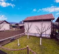 A garden with a cottage in Partizánske, fruit trees and cultivated land, clear sky.