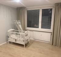 A crib in a 3-room apartment with a wood-patterned floor and gray curtains.