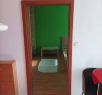 A room with a bed, green wall, wooden decor flooring, furniture in a studio apartment.
