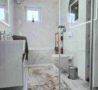 A bathroom in a family house with marble tiles, a mirror, and a shower enclosure.