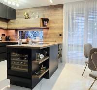 A kitchen in a family house with an island, black cabinets, and a wine cooler.