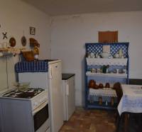 A kitchen in a family house with traditional furniture and decorations, and a wooden-patterned floor.