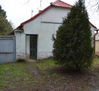 A family house in Abrahám with a red roof, a green gate, and a tree in the yard.
