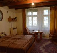 A room in a family house with a bed, chairs, yellow curtains, and a carpet.