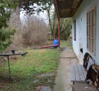 The garden of a family house in Abrahám with a bench, green area, and trees.