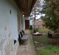 A family house in Abrahám with a bench on a damaged concrete walkway and an overgrown garden.