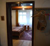 Interior of a family house with a bed and wooden floor, a room is visible through the door.