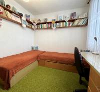 A room in a 3-room apartment with shelves full of books and a simple desk.