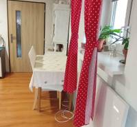A dining room in a family house with a red curtain, a table, and a wooden-patterned floor.