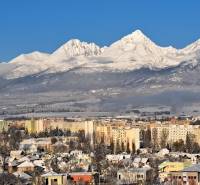 Snow-covered mountains with a view of part of the city of Poprad and multi-story buildings.