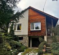 A cottage in Modra with wooden cladding and a garage, surrounded by greenery.