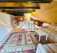 The attic of a cottage with a sofa, a hammock, and a wooden decor floor.