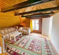 The attic of the cottage with a wooden ceiling, a striped sofa, and a hanging swing chair.