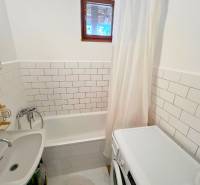 A bathroom in a cottage with a bathtub, a washing machine, and white tiles.