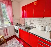 A small kitchen in a cottage with red cabinets, tiles, and appliances.