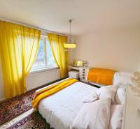 A bright bedroom in a cabin with white walls, yellow curtains, and a carpet.