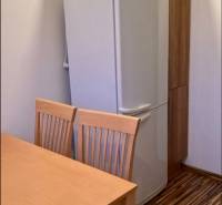 Kitchen in a 3-room apartment with a refrigerator, wooden table and chairs, floor with wooden decor.
