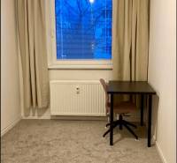 A room in a 3-room apartment with a desk and carpeted floor.
