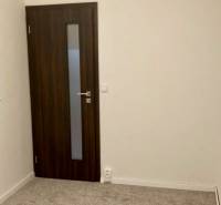 A room in a 3-room apartment with carpet flooring and dark doors.