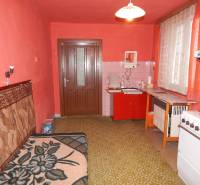A kitchen in a family house with red walls, older furniture, and a green carpet.