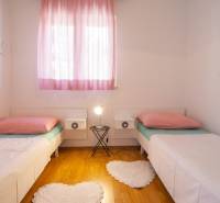 A bright bedroom with two beds, pink curtains, and a wood-patterned floor.