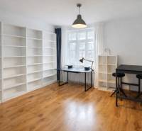 A spacious room with shelves, a table, and a wooden-patterned floor in a two-room apartment.