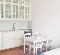 A kitchenette with white furniture, a table, and a crystal chandelier in a studio apartment.