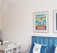 Interior of a 1-room apartment with a kitchen, chandelier, and paintings above a blue bed.