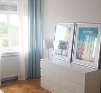 A bedroom in a studio apartment with a cabinet, chandelier, and wooden decor flooring.