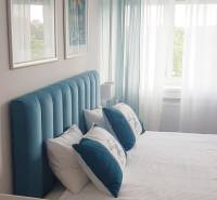 Bedroom in a studio apartment with a bed, turquoise headboard, paintings, and light curtains.