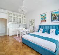 A one-bedroom apartment with a wood-patterned floor, a bed, and white kitchen cabinets.