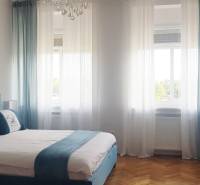 A bedroom with a double bed, paintings, and a wooden decor floor in a studio apartment.