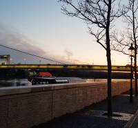 An evening view of the UFO Bridge from Rázus Embankment in Bratislava, with an illuminated walkway.