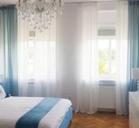 Bright bedroom in a one-room apartment with wood-patterned flooring and turquoise curtains.