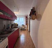A kitchen in a two-room apartment with a wooden decor floor, with a dining area in the background.