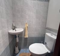 A bathroom in a 2-room apartment with a toilet and a sink, surrounded by light tiles.