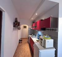 A kitchen with red cabinets and a wood-patterned floor in a two-room apartment.