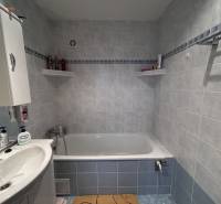 A bathroom with a bathtub, sink, and shelves in a 2-room apartment with blue tiles.
